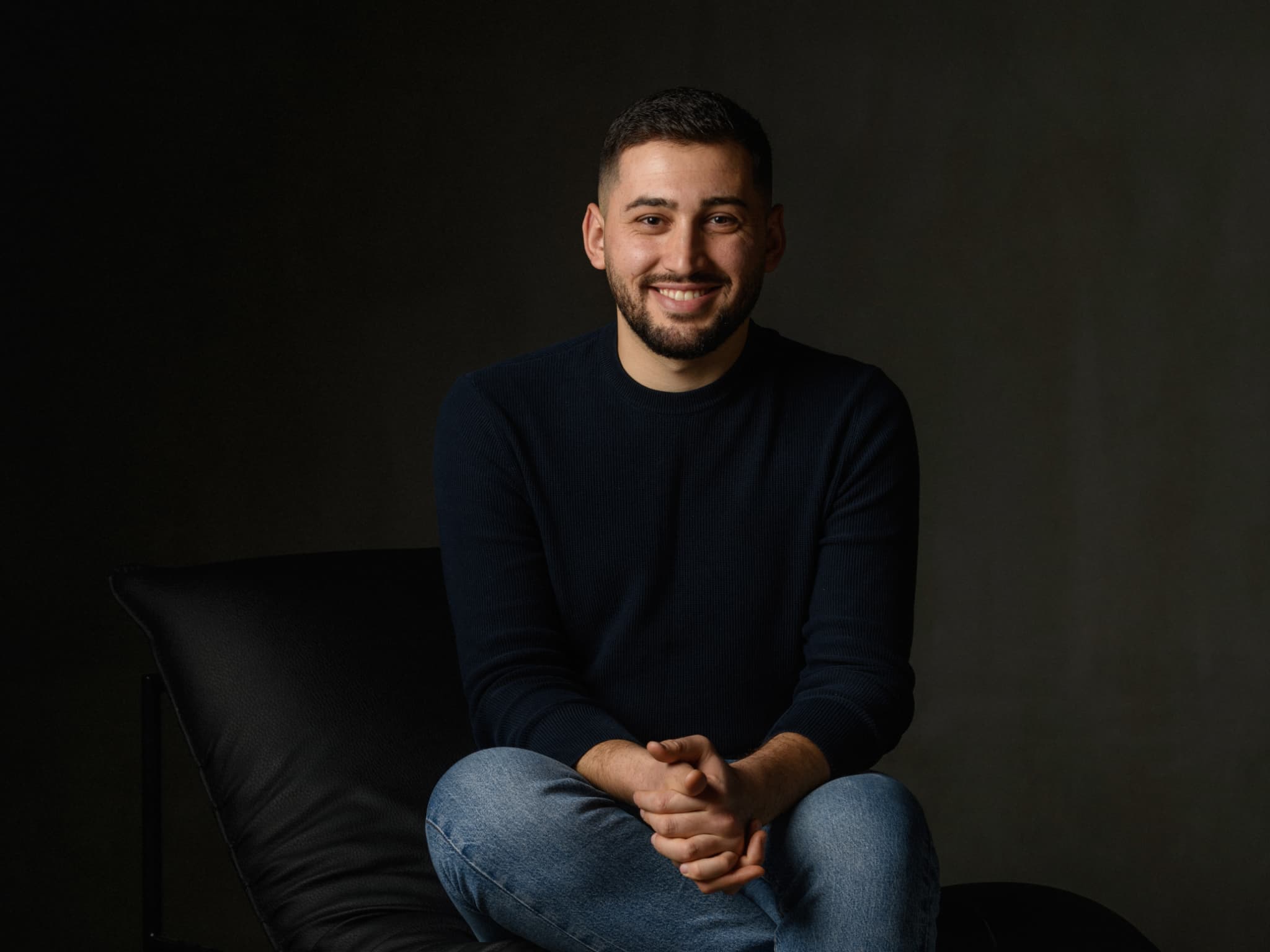 Portrait photo with moody lighting, person seated and smiling